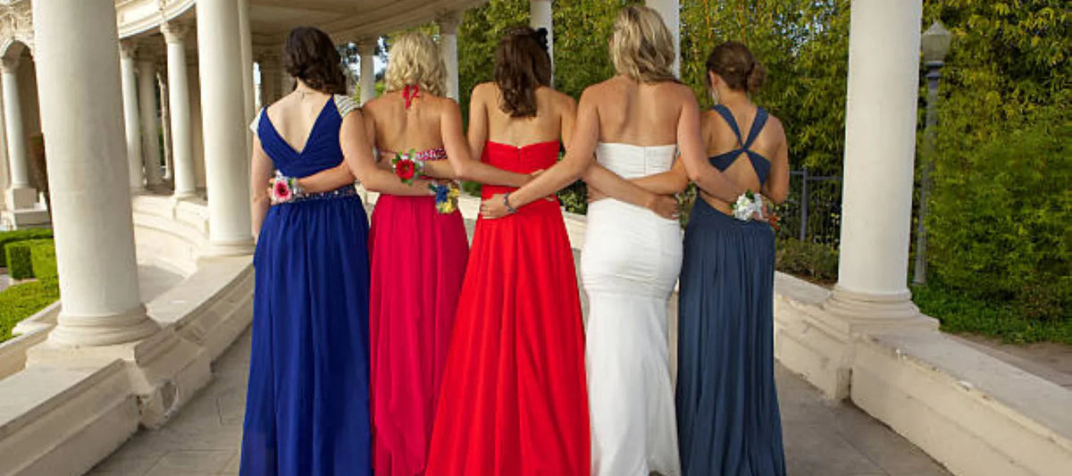 Cinq femmes en robes de soirée longues et colorées, bras dessus bras dessous, en extérieur