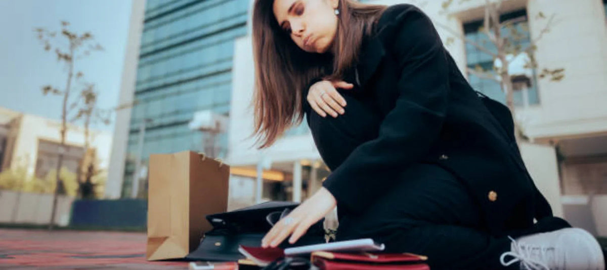 Femme assise dehors avec sacs à main et accessoires mode éparpillés sur le sol.