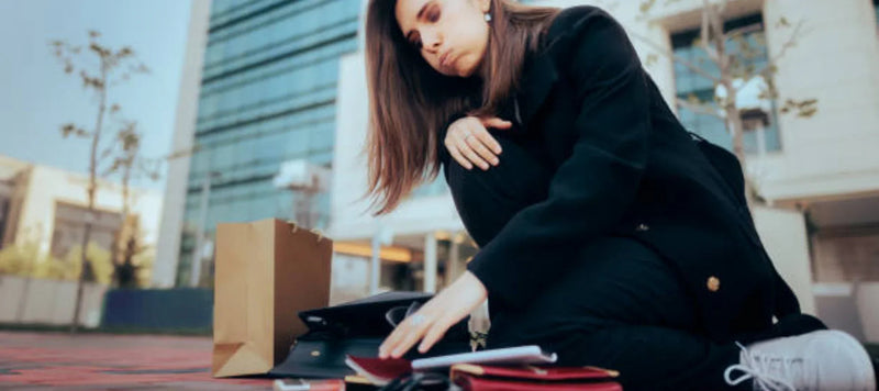Femme assise dehors avec sacs à main et accessoires mode éparpillés sur le sol.