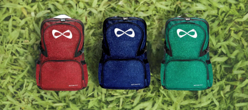 Trois sacs à dos tendance rouge, bleu et vert posés sur de l’herbe, accessoires mode femme.