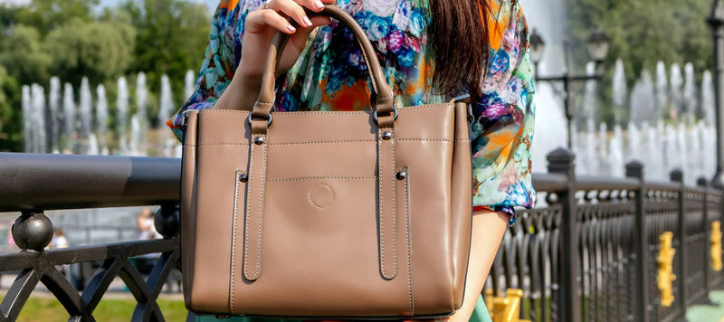 Sac à main femme en cuir beige, porté devant une fontaine, accessoire de mode élégant