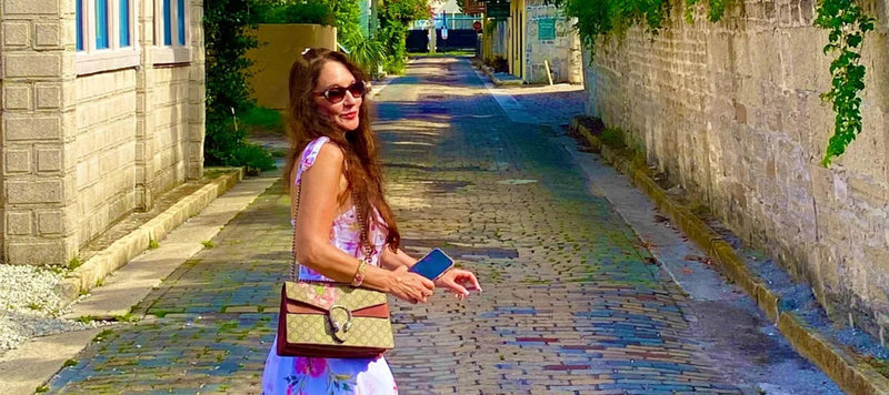 Femme élégante en robe fleurie tenant un sac à main tendance sur une rue pavée au soleil