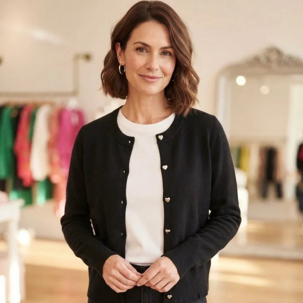 Femme portant un cardigan noir boutonné sur un t-shirt blanc dans une boutique de mode.