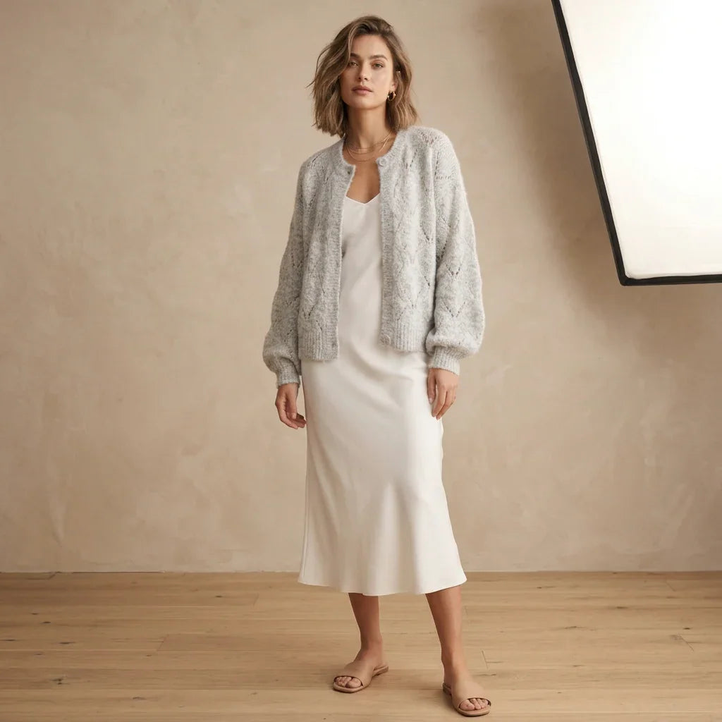 Femme portant un cardigan ajouré gris C'est Elle sur une robe longue blanche.