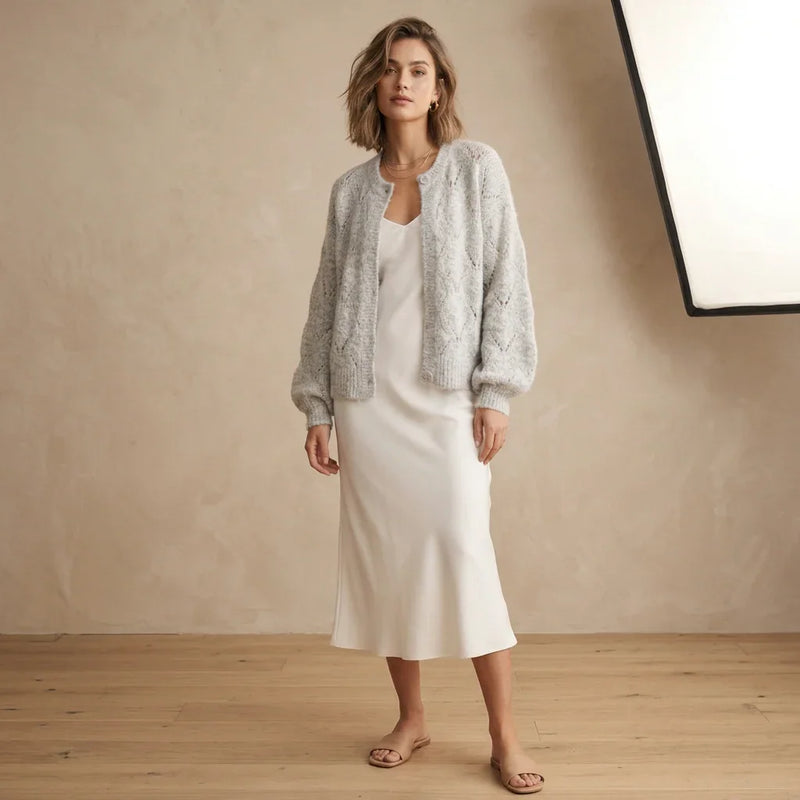 Femme portant un cardigan ajouré gris C'est Elle sur une robe longue blanche.