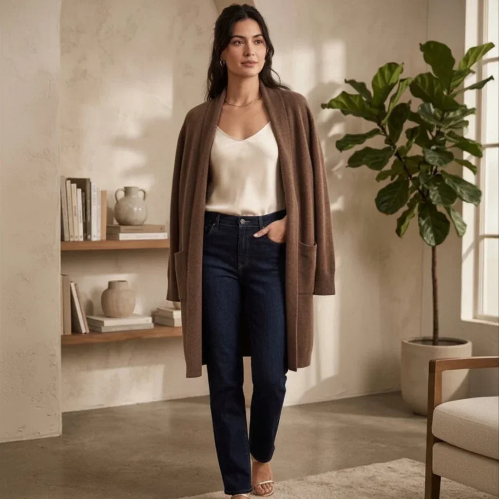 Femme portant un long gilet marron, un top blanc et un jean bleu foncé.