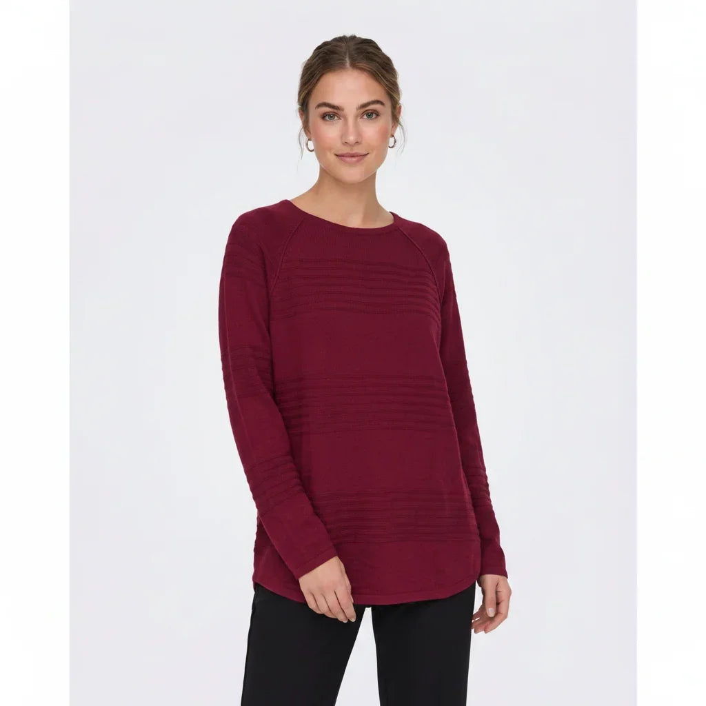 Femme portant un chandail à manches longues bordeaux avec textures rayées et pantalon noir.