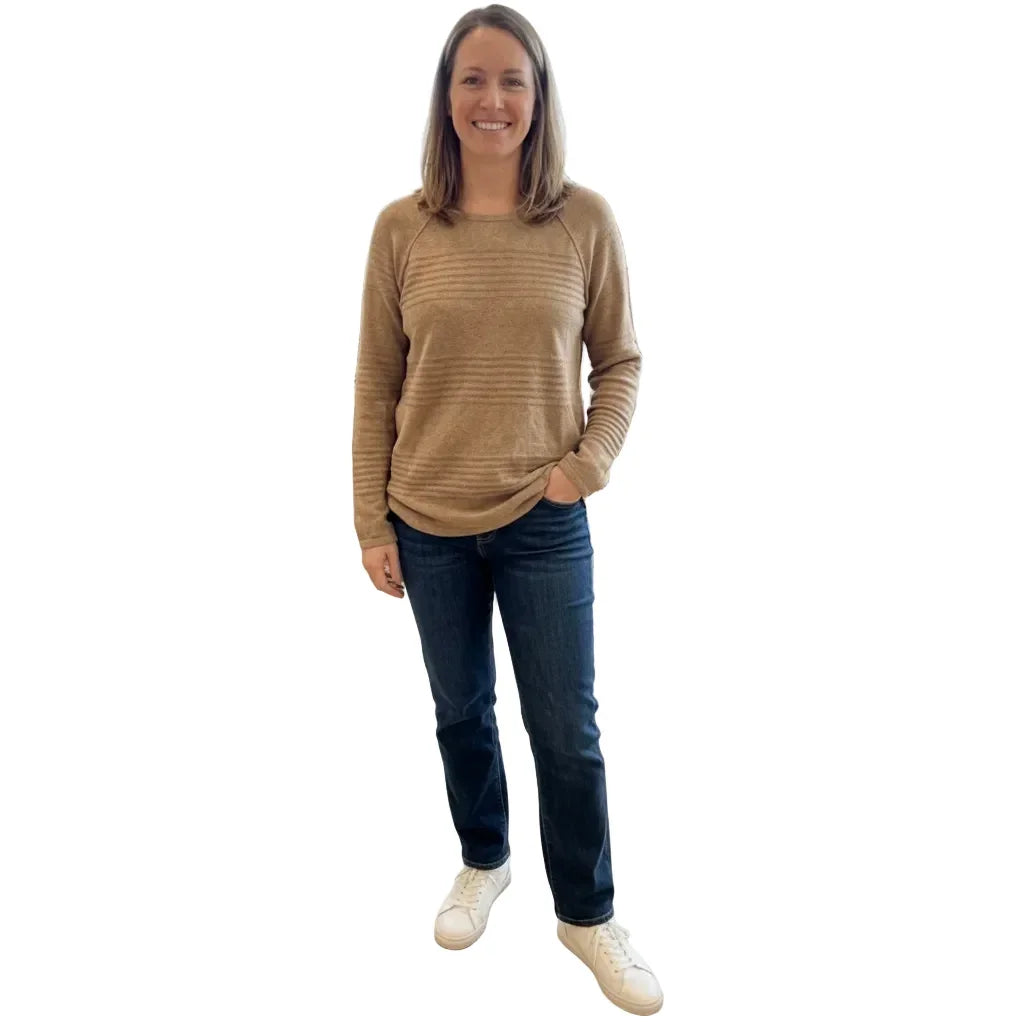 Femme portant un pull beige texturé et un jean bleu foncé avec des baskets blanches.