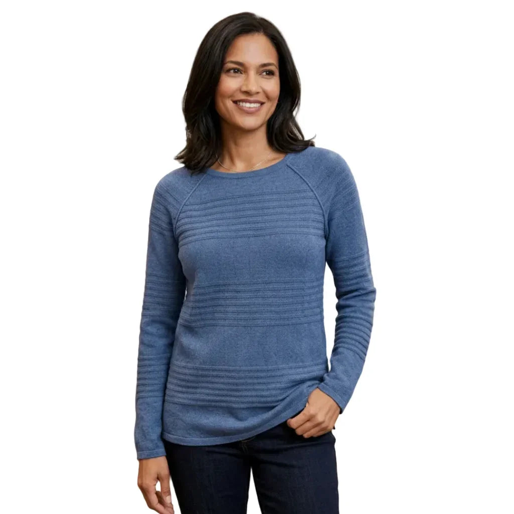 Femme souriante portant un pull bleu à manches longues avec détails texturés et un jean foncé.