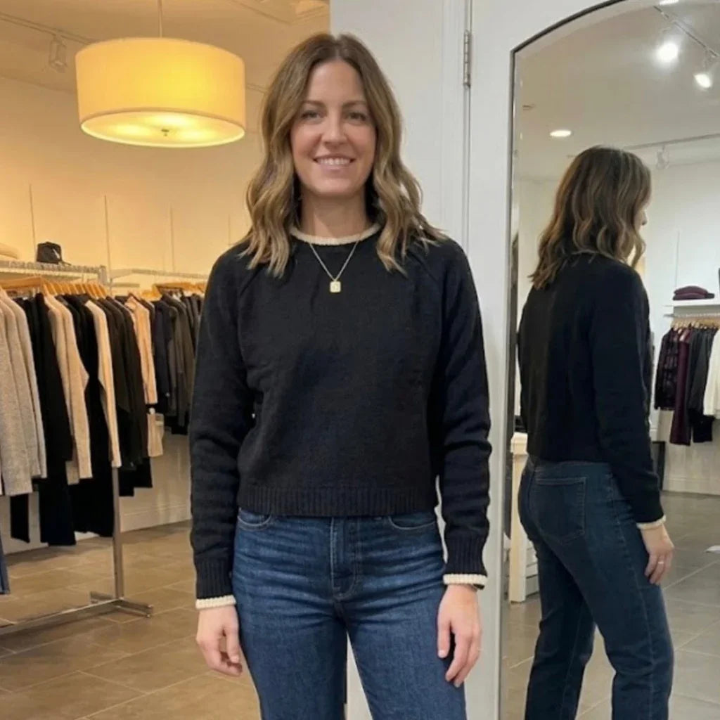 Femme portant un chandail noir C'est Elle avec bordures blanches et jean bleu.