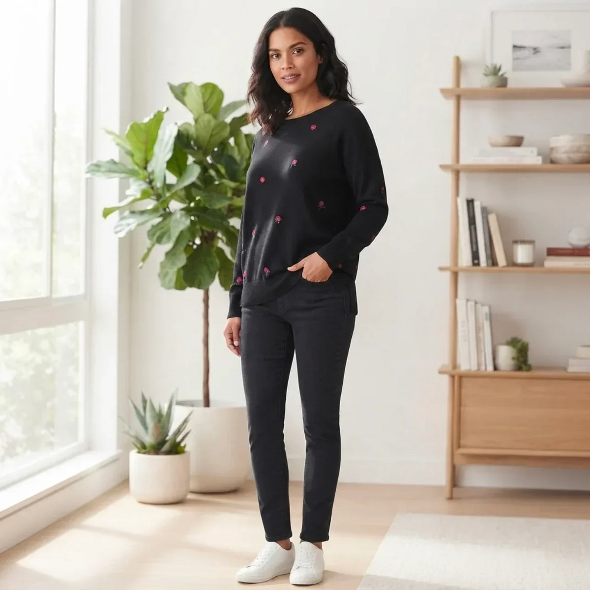 Femme portant un chandail noir brodé de fleurs C'est Elle et un jean noir ajusté.
