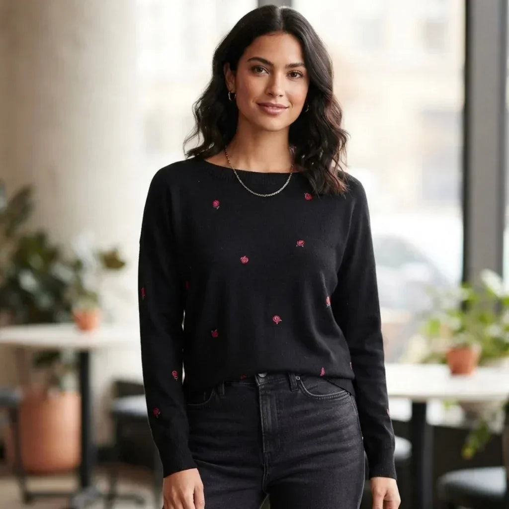 Femme portant un chandail noir brodé de fleurs rouges de C'est Elle et un jean noir.