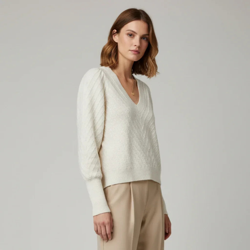 Femme portant un pull blanc cassé à col en V et manches bouffantes avec un pantalon beige.
