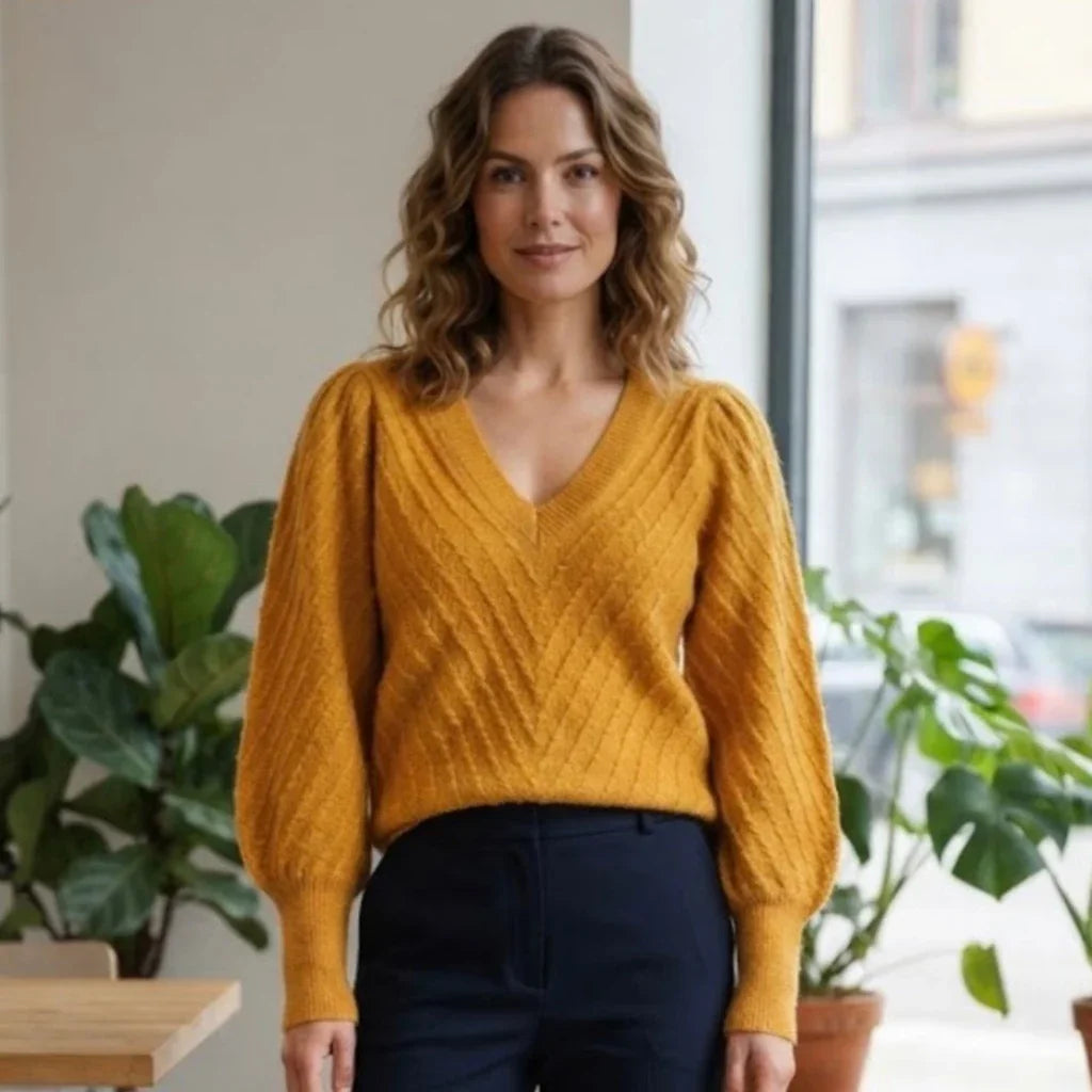 Femme portant un pull en maille jaune moutarde à col en V et pantalon bleu marine.