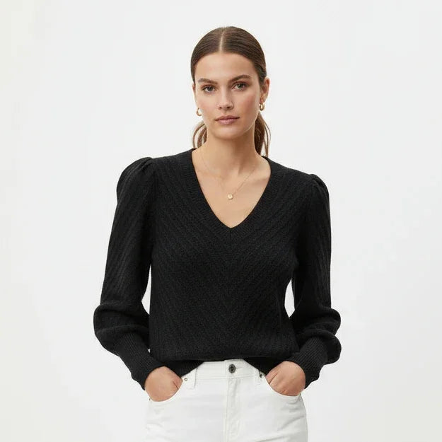 Femme portant un pull noir à col en V et manches bouffantes avec un pantalon blanc.