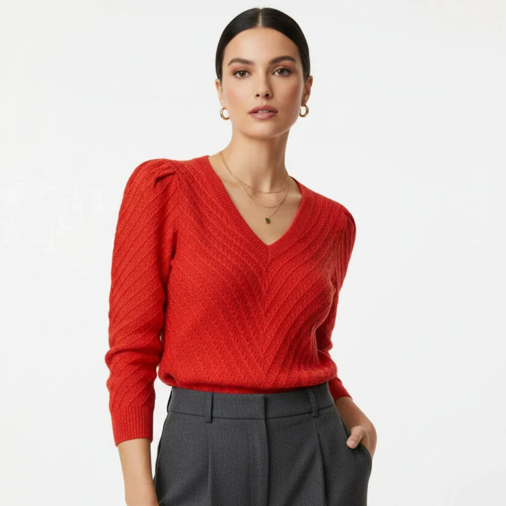 Femme portant un pull rouge à col en V et manches bouffantes avec un pantalon gris.