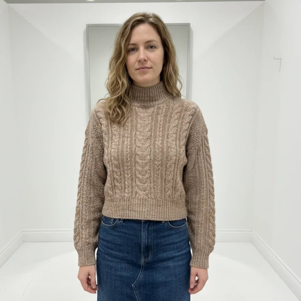 Femme portant un pull beige à torsades et une jupe en jean bleue.