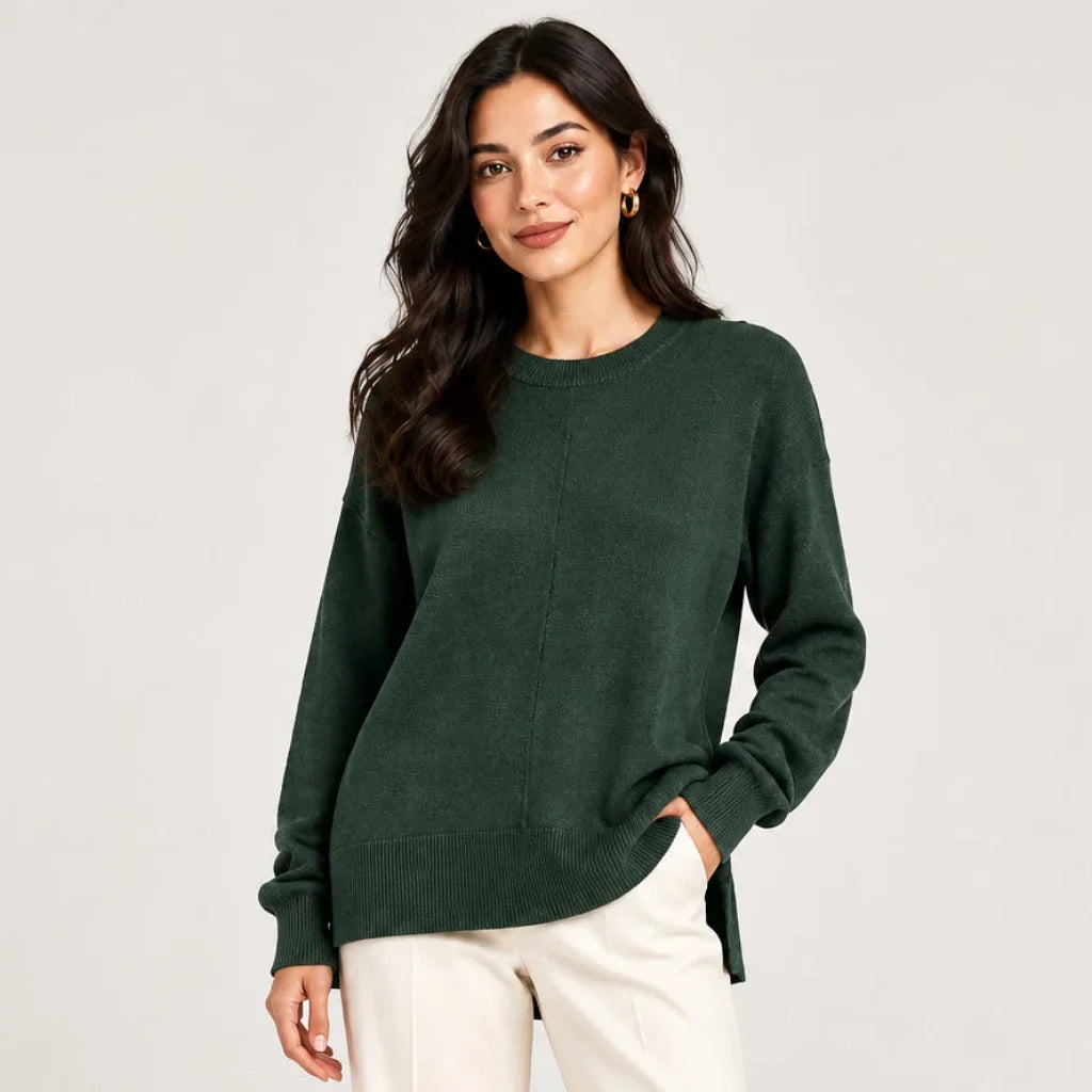 Femme portant un chandail essentials vert foncé C'est Elle et un pantalon blanc.