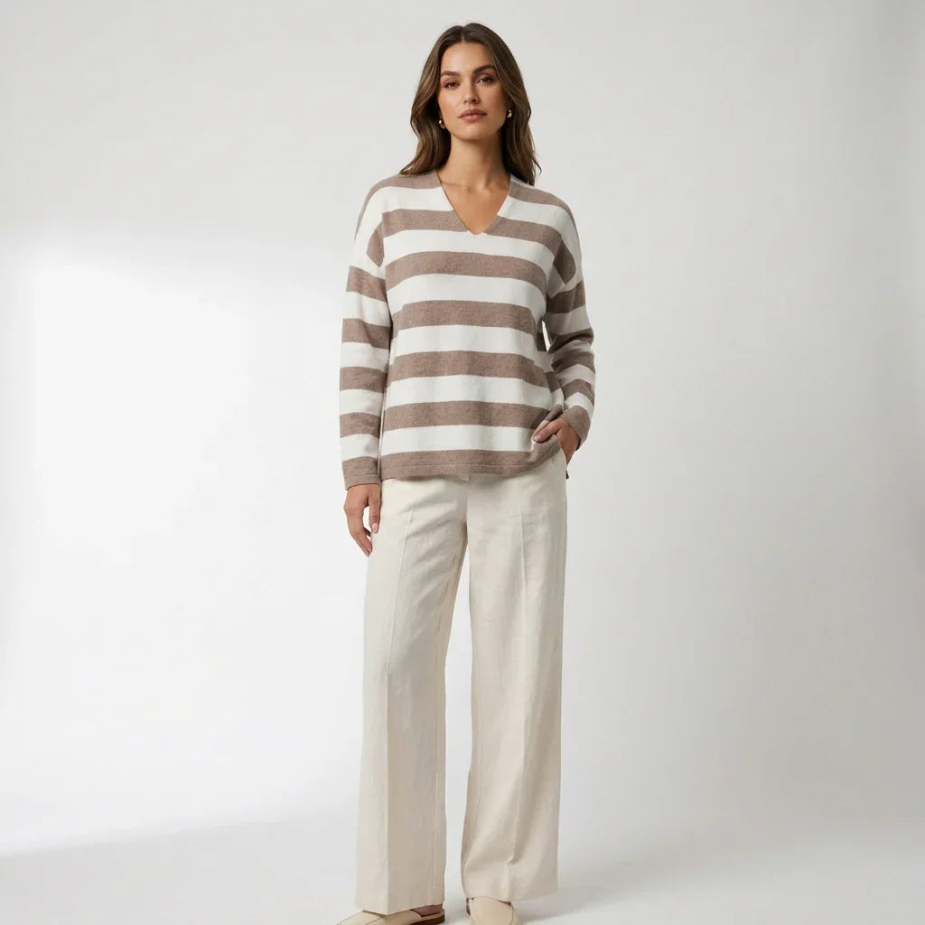 Femme portant un chandail en maille douce à rayures beige et blanc C'est Elle et un pantalon blanc.