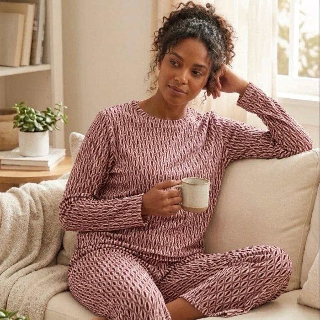 Femme portant un ensemble pyjama rose à motifs géométriques, tenant une tasse sur un canapé.