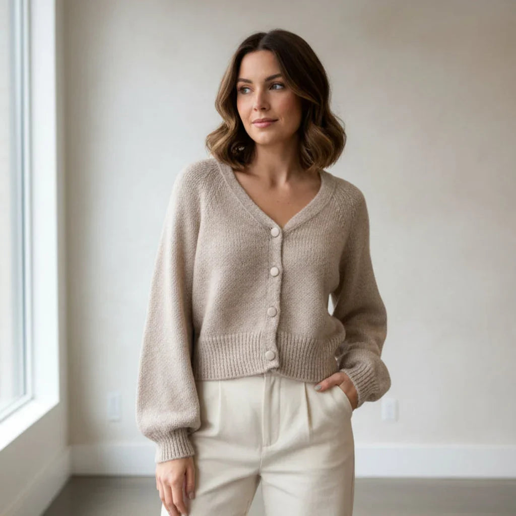 Femme portant un cardigan en maille beige boutonné et un pantalon blanc crème.