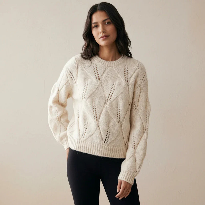 Femme portant un pull en maille torsadée blanc cassé et un pantalon noir.
