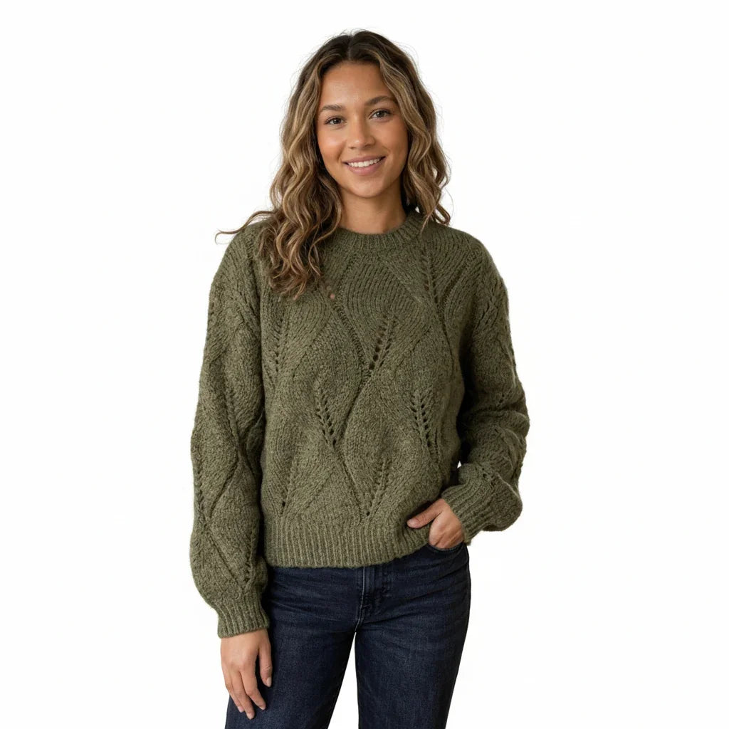 Femme portant un pull en maille torsadée vert olive et un jean bleu foncé.