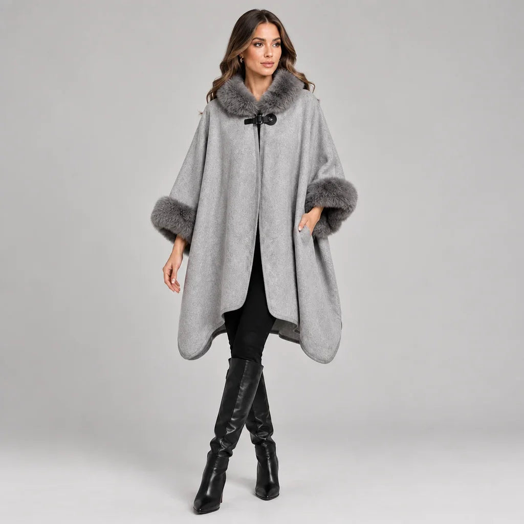 Femme portant un poncho gris C'est Elle avec bordures en fourrure et bottes noires.