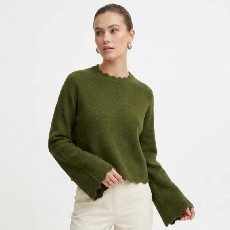 Femme portant un pull col festonné vert olive de C'est Elle et un pantalon blanc.