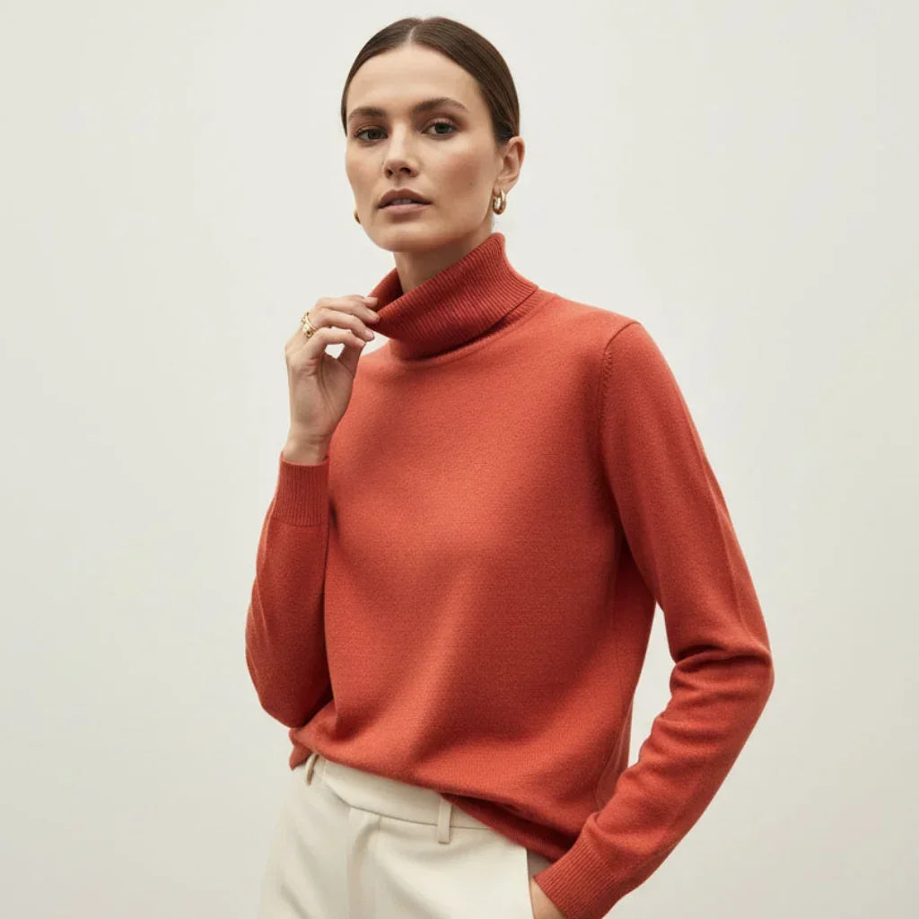 Femme portant un pull à col roulé orange terracotta et un pantalon blanc.