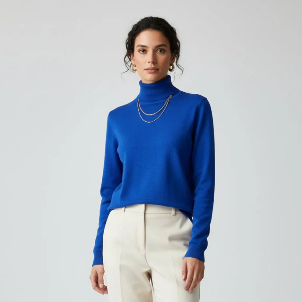 Femme portant un pull à col roulé bleu royal et un pantalon blanc cassé.