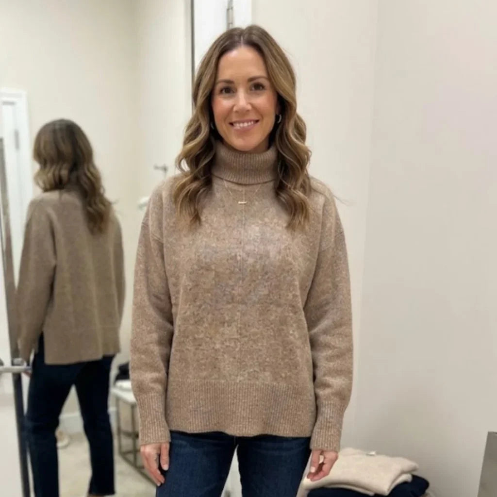 Femme portant un pull col roulé ample beige C'est Elle avec un jean bleu.