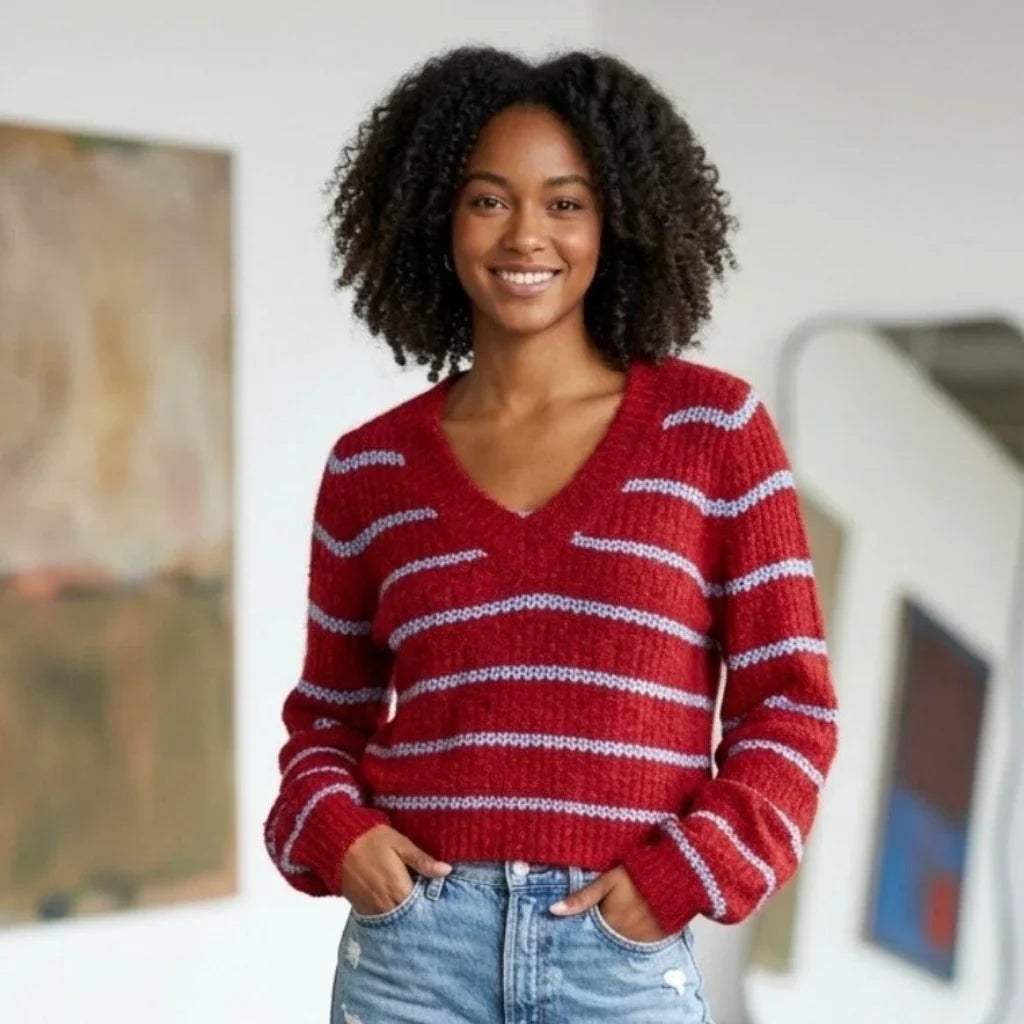 Femme souriante portant un pull en maille rouge à rayures bleues et un jean bleu.