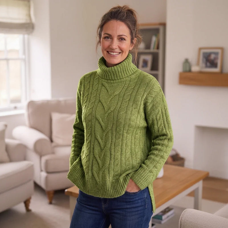 Femme souriante portant un pull à col montant en maille torsadée vert pomme et un jean bleu.